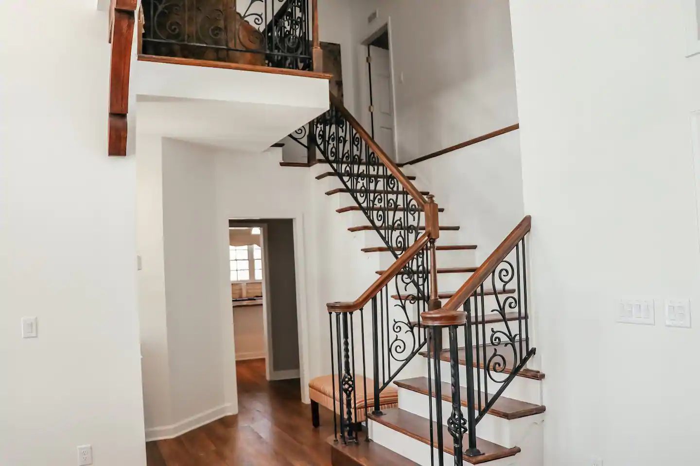 Modern staircase with black wrought-iron railing and wood steps in a bright white foyer