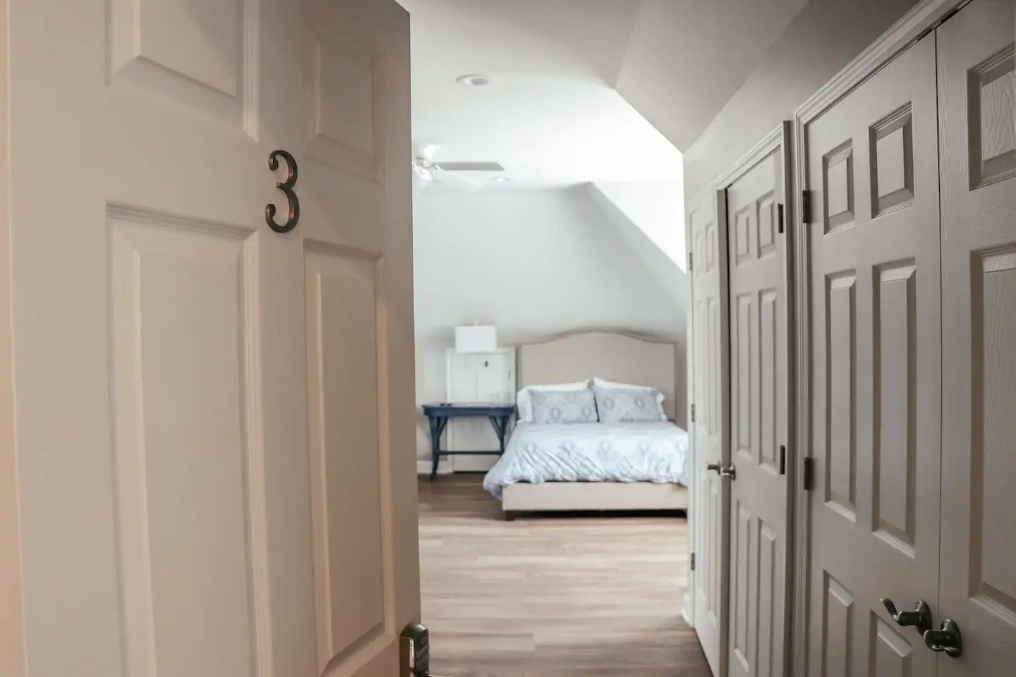 Open bedroom door framing a bright, neatly made bed at the end of a hallway