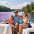 Family smiling on a boat on a lake, with trees and cloudy sky in the background