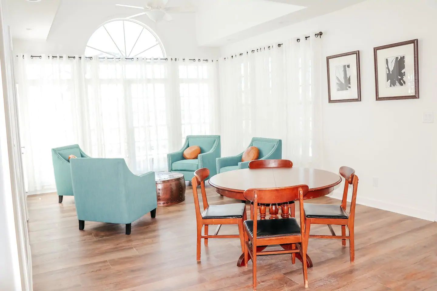Bright white living room with turquoise chairs, wooden table, and light wood floors by tall windows