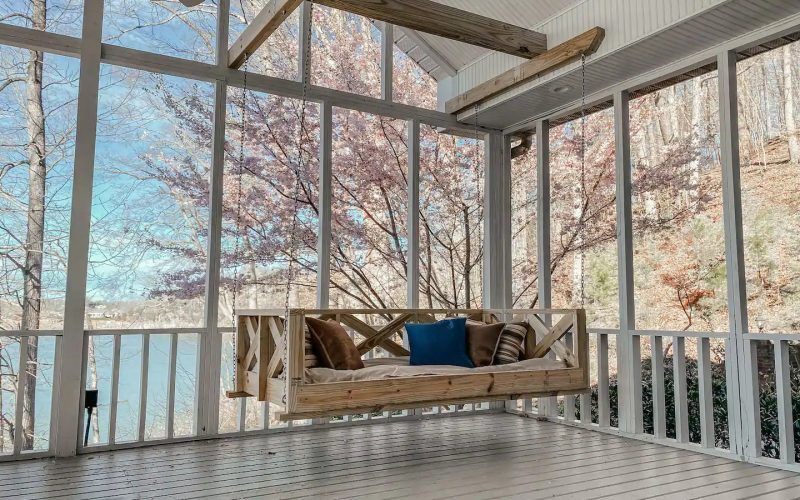 Covered porch with a hanging chair and blue cushion overlooking leafless trees in winter