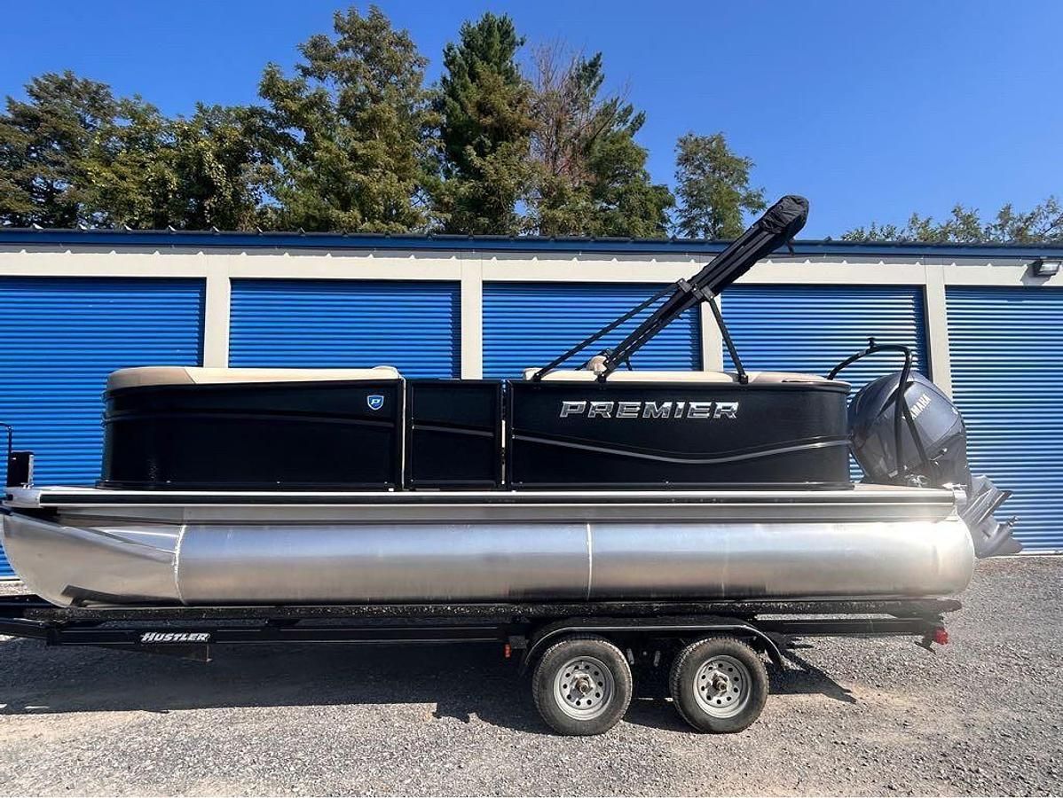 Black and silver pontoon boat on a trailer in front of blue storage units