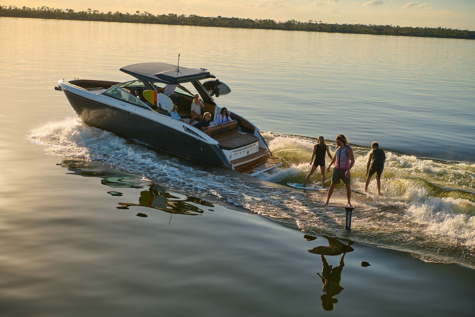 3 young men wake surfing off the back of a brand new Malibu Wakeboard boat.