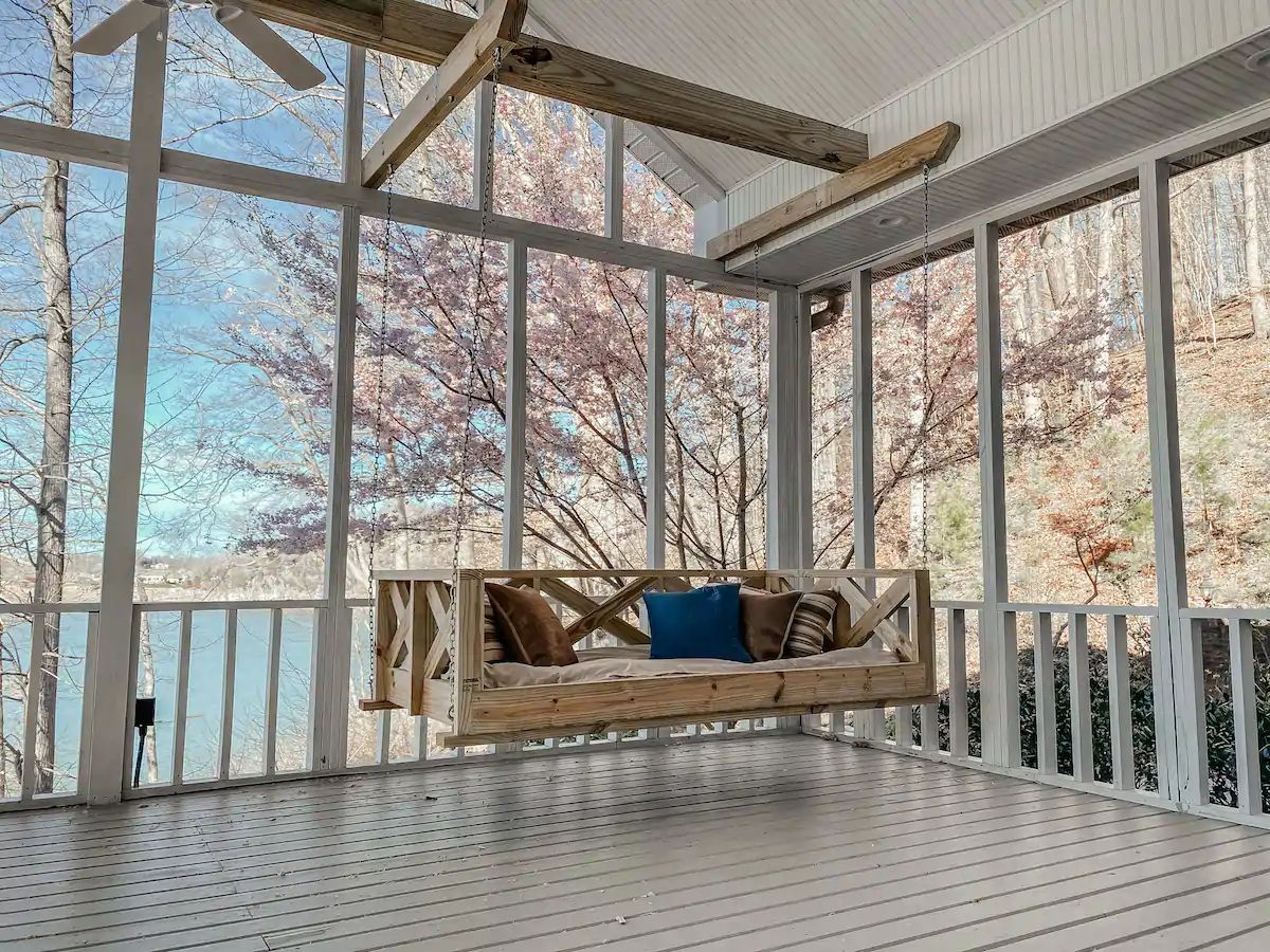 Screened porch with a hanging wooden swing, patterned floor, and snowy trees outside