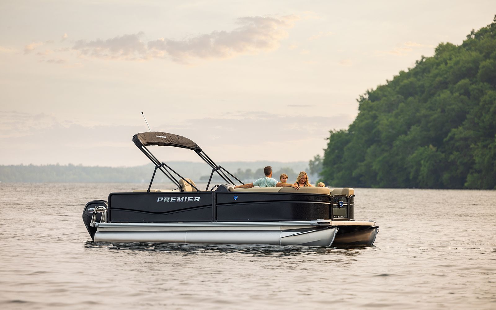 Rent This Boat! Black pontoon boat cruising on calm water near a green shoreline at sunset