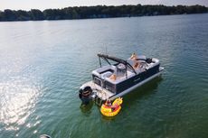 Three people in life vests jumping off a pontoon boat into a lake, smiling and splashing water