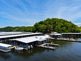 Explore More About What We Do! Marina with white-roofed docks and boats on calm water beside a lush green shoreline