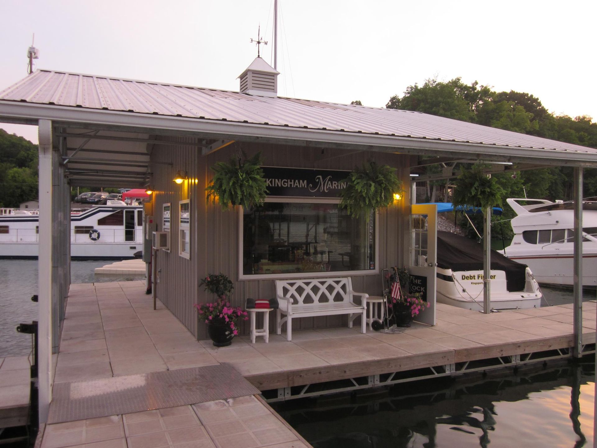 Check out the store! Small waterfront boathouse with a metal roof and docked boats at sunset