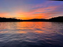 Explore Our Products & Services Orange sunset over a calm lake with rippling water and silhouetted tree-lined shores