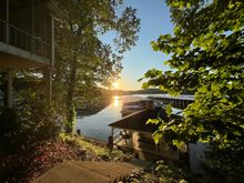 Get a slip! Sunset over a lakeside dock framed by trees and a house, with sunlight reflecting on the water