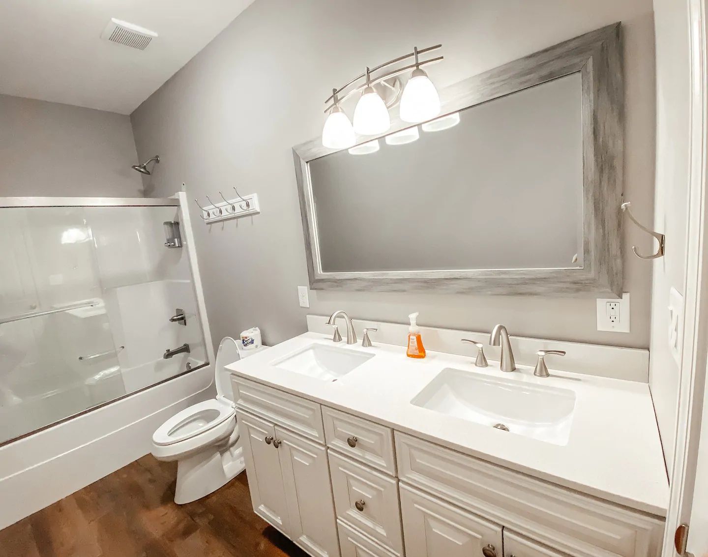 Bright bathroom with double vanity, large mirror, tub-shower combo, and wood-look floor.