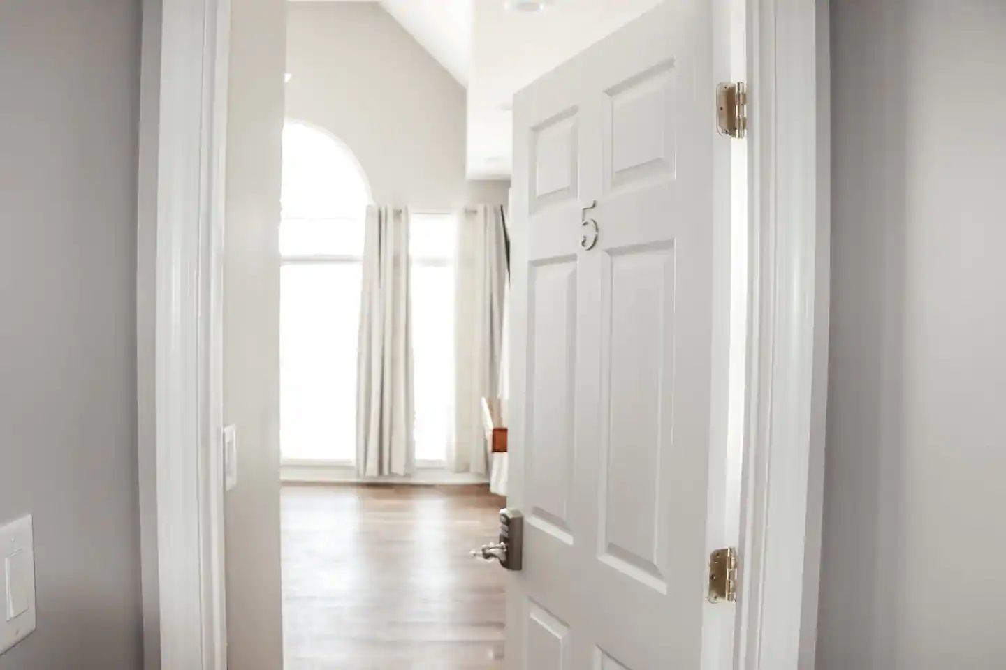 Bright hallway view into a sunlit room with tall windows and an open white door