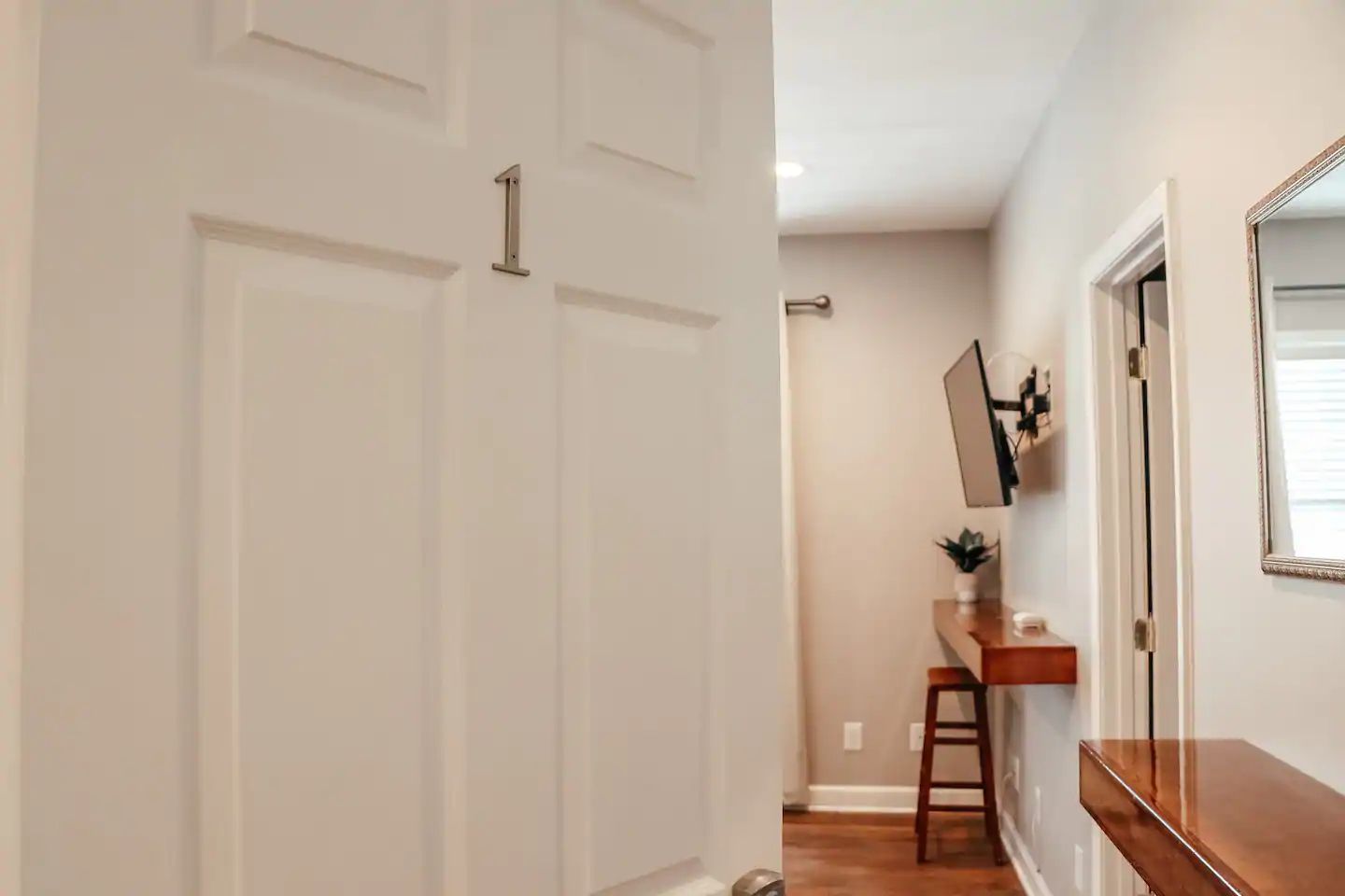 Hallway with open white door, console table, wall mirror, and wood floors.