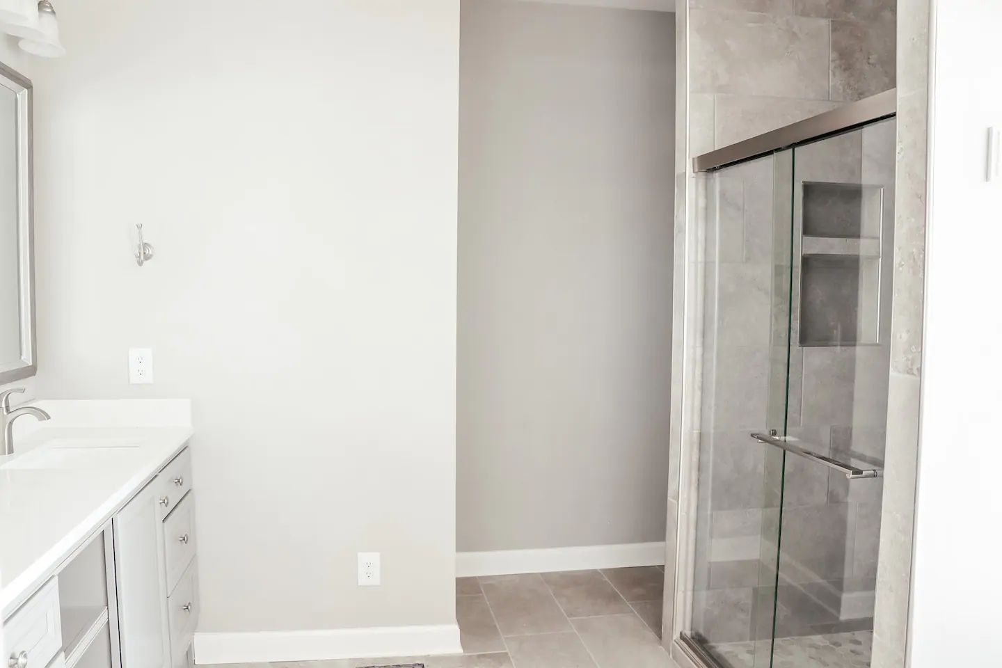 Empty bathroom with white vanity, gray walls, light tile floor, and glass shower enclosure.