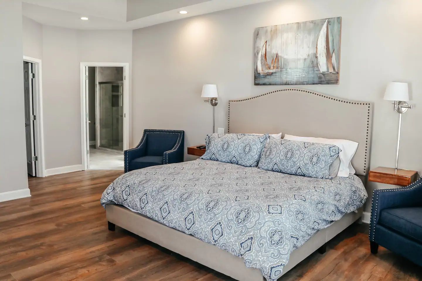 Modern bedroom with gray upholstered bed, blue chairs, wood floor, and soft neutral decor
