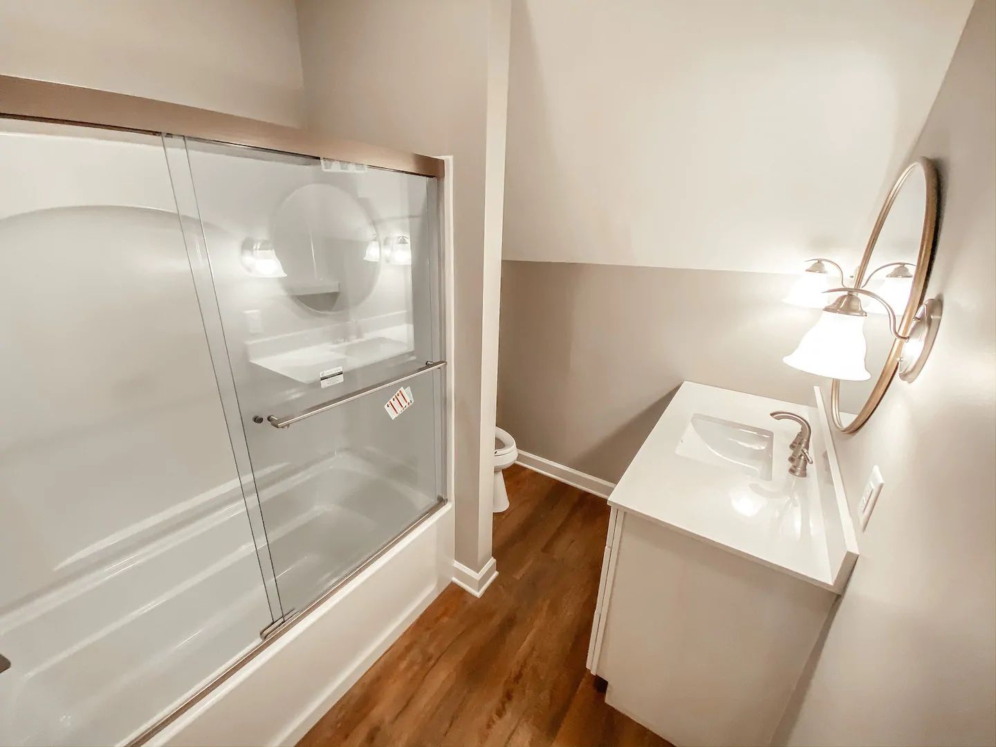Modern bathroom with a glass shower, white vanity, round mirror, and wood-look floor
