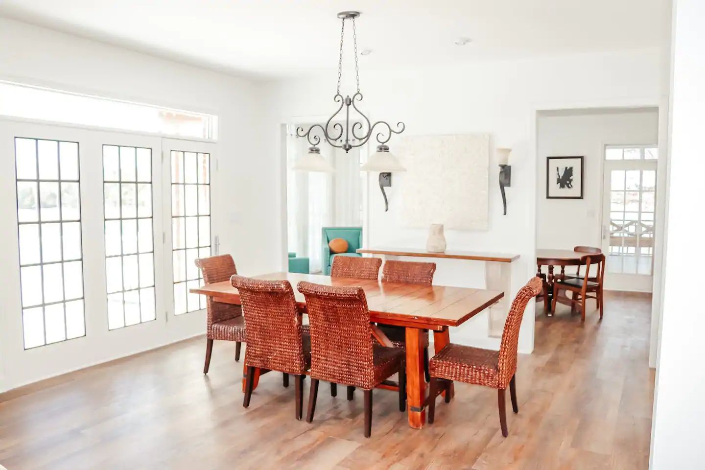 Bright dining room with a wooden table, orange chairs, chandelier, and large windows.