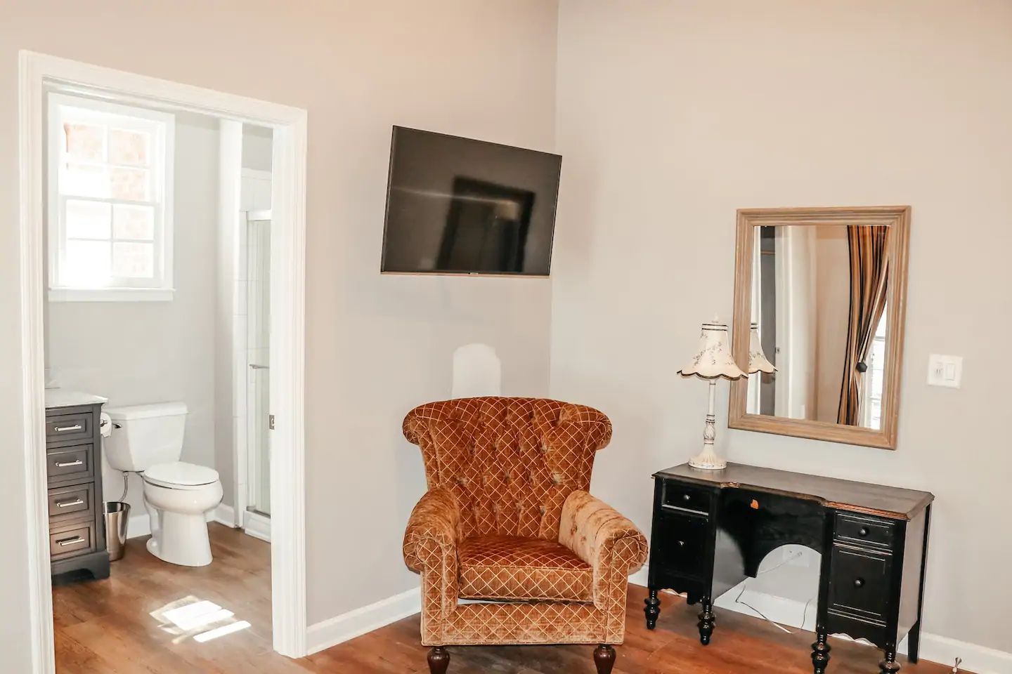Small room with wall-mounted TV, armchair, vanity, and open bathroom doorway