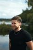 Smiling man in a black T-shirt standing outdoors near a lake and trees