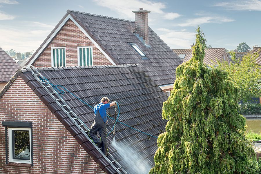 A man is cleaning the roof of a house with a high pressure washer.