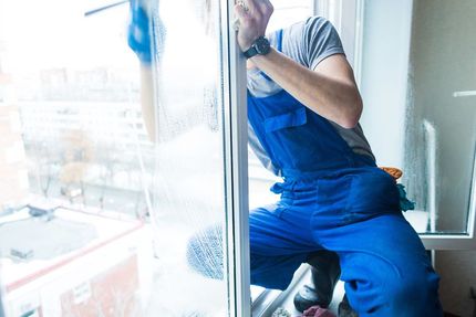 A man in blue overalls is cleaning a window with a squeegee.