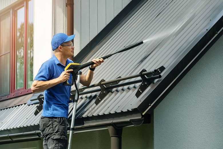 A man is cleaning the roof of a house with a high pressure washer.