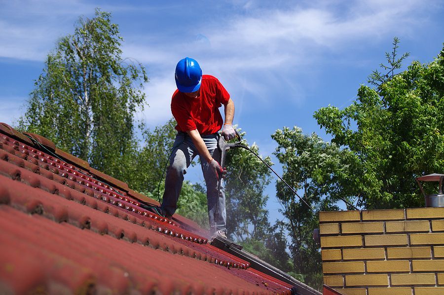 A man wearing a blue hard hat is cleaning a red roof