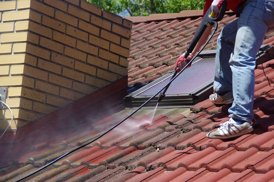 A man is cleaning a roof with a high pressure washer
