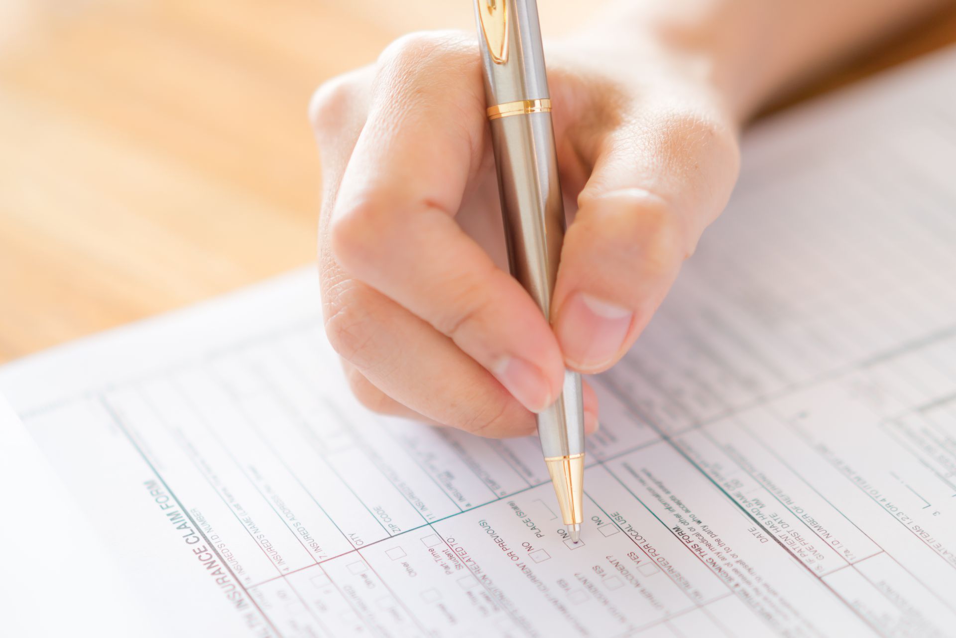 Hand holding a silver pen, writing on a form.
