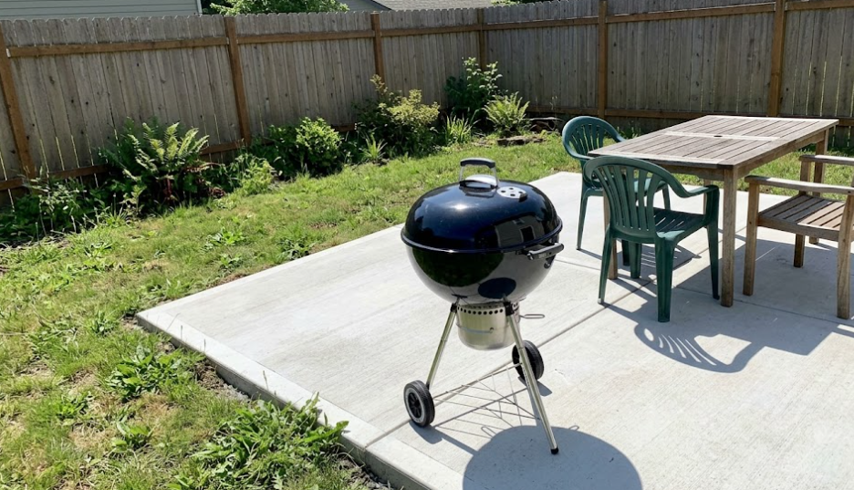 A beautiful new broom-finish concrete patio in a Kennewick backyard featuring a BBQ grill and dining table.