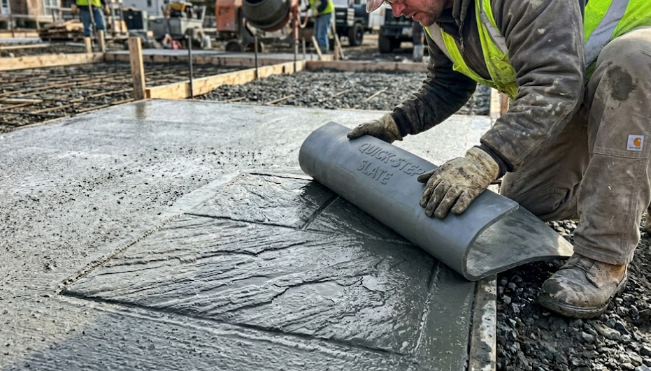 A construction worker presses a textured mat into wet concrete to create a patterned finish on a patio.