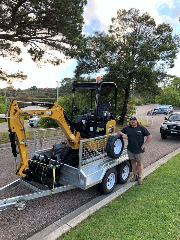 A man is standing next to a small excavator on a trailer.