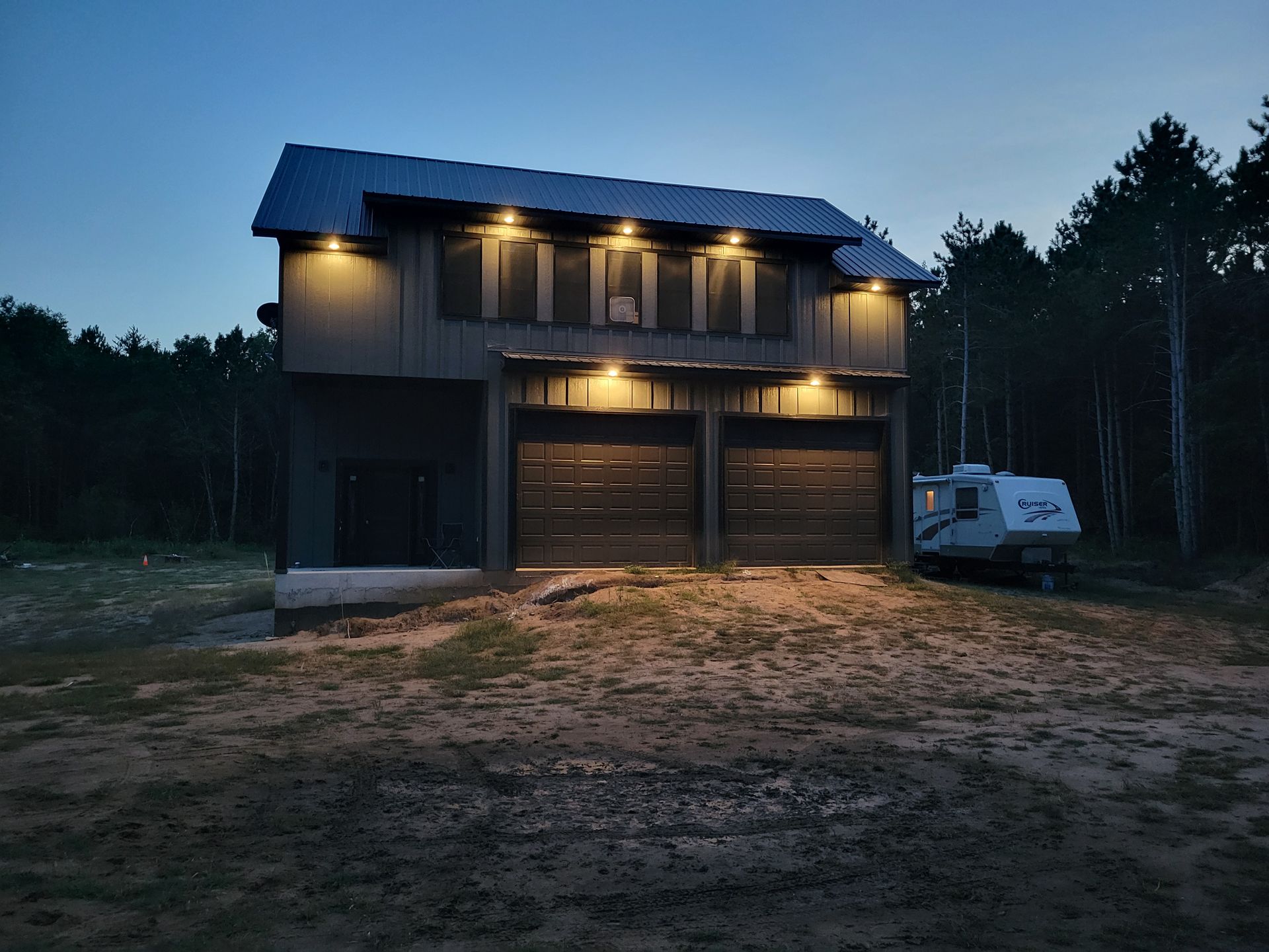 Modern building exterior with large windows, illuminated at dusk. Gray facade, entry with overhead lighting.