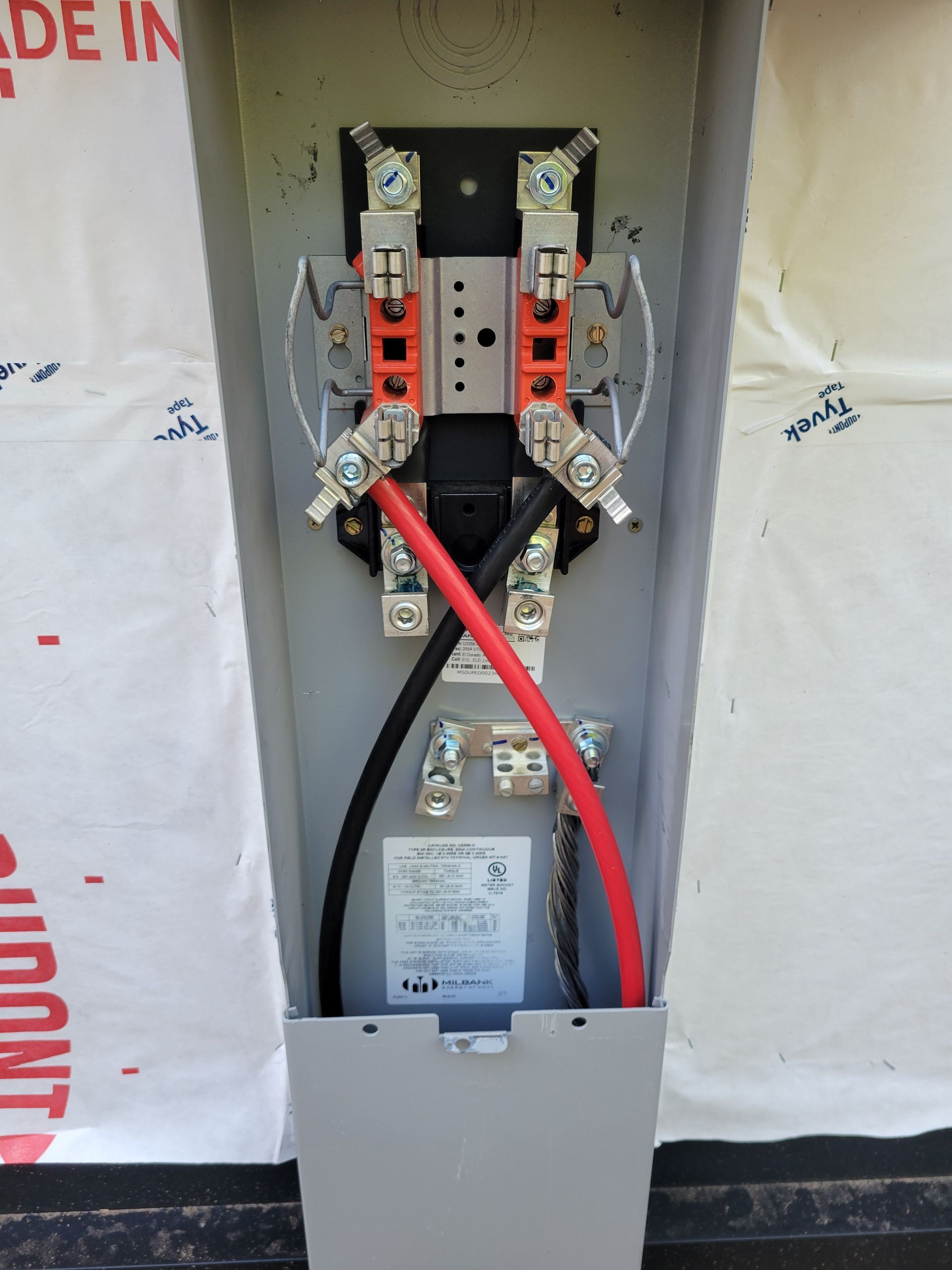 Electrician using a multimeter on electrical panel, wearing gloves. Meter reads 390.