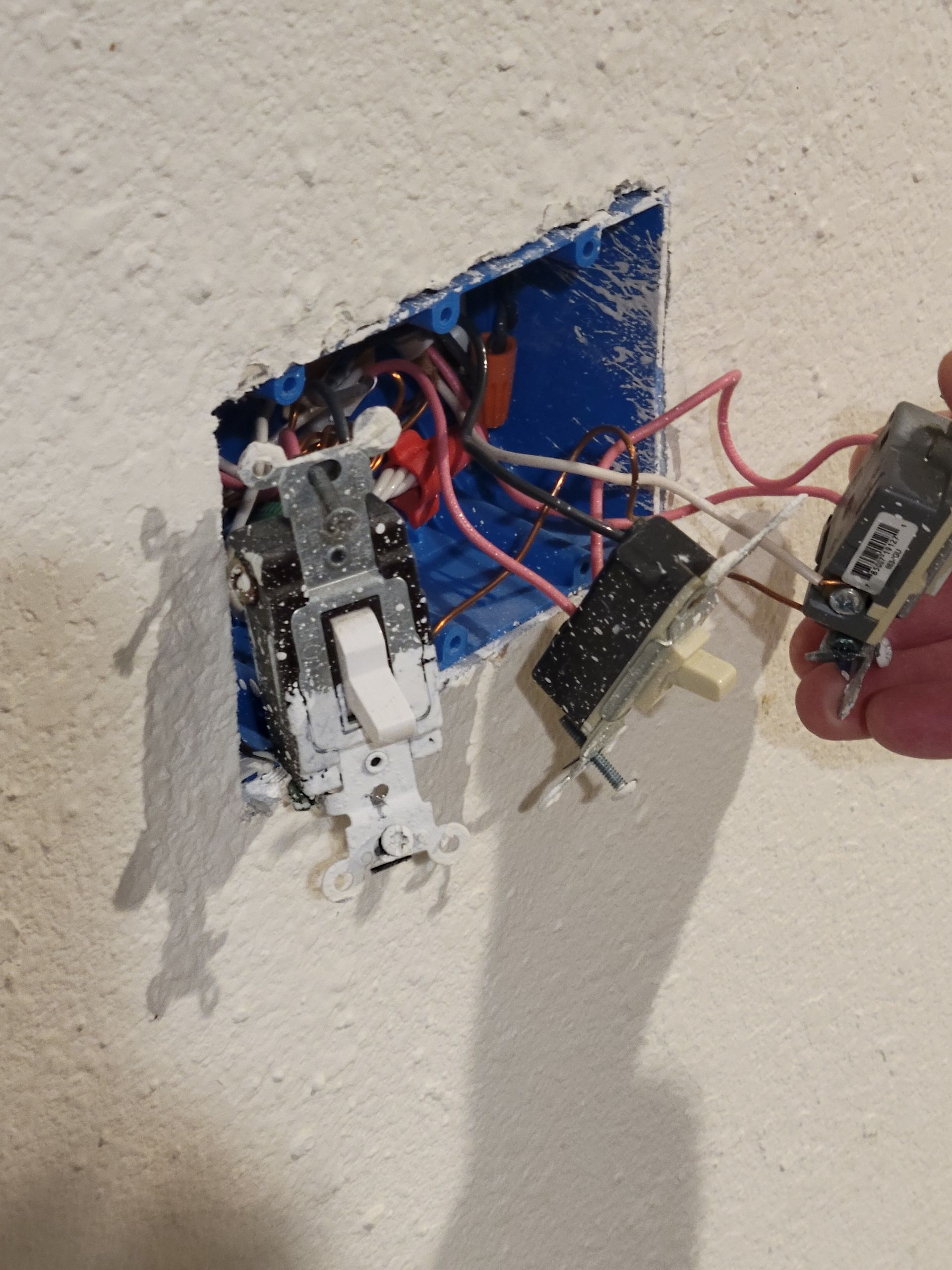 Electrician in blue shirt, reflective stripes, gray pants, works on electrical panel inside office. Ladder nearby.