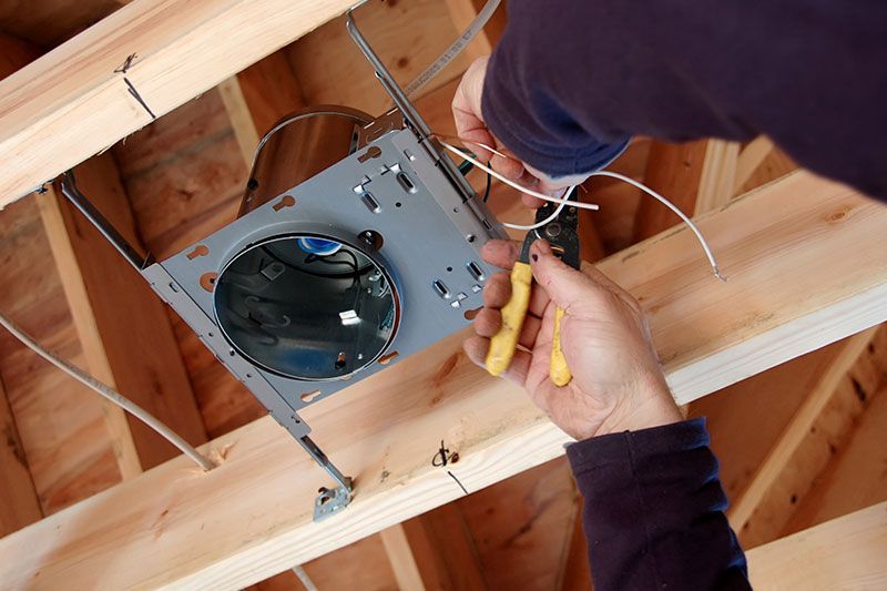 Electrician working on electrical panel, wearing safety vest and glasses. Indoors, office setting.