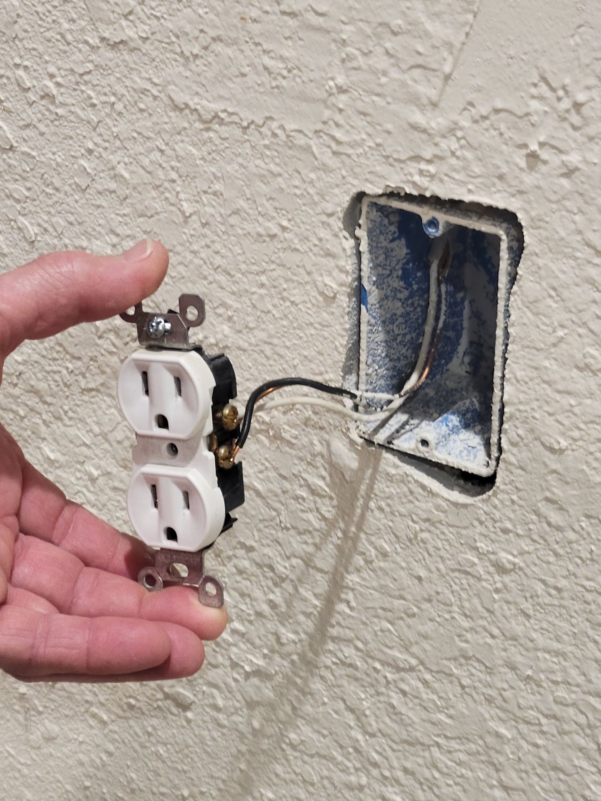 Electrician in yellow helmet, working on wires in a wall-mounted box inside an office.