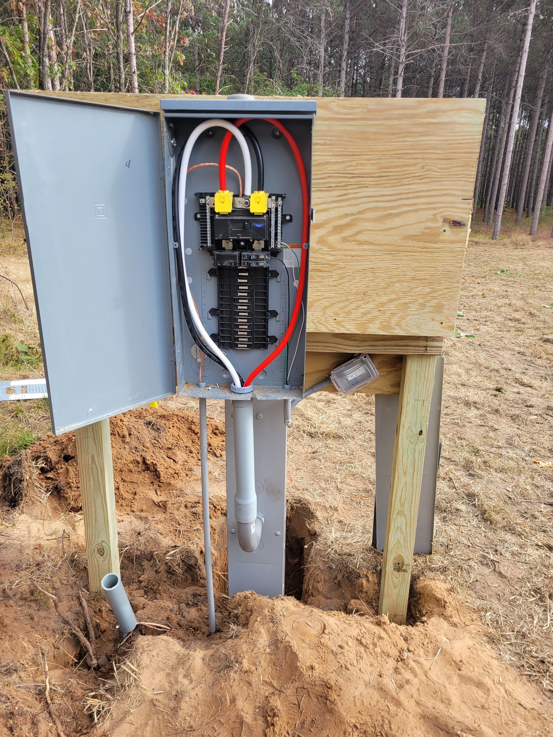 Electrician in blue coveralls using a multimeter on an electrical panel in a home, wearing safety glasses.