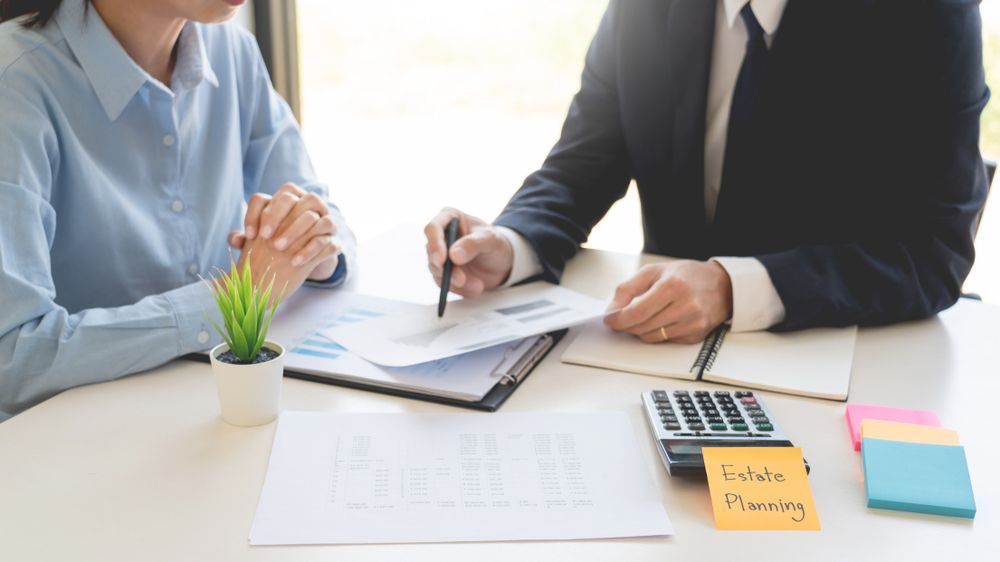 A person in a suit points at a document for another person at a desk;