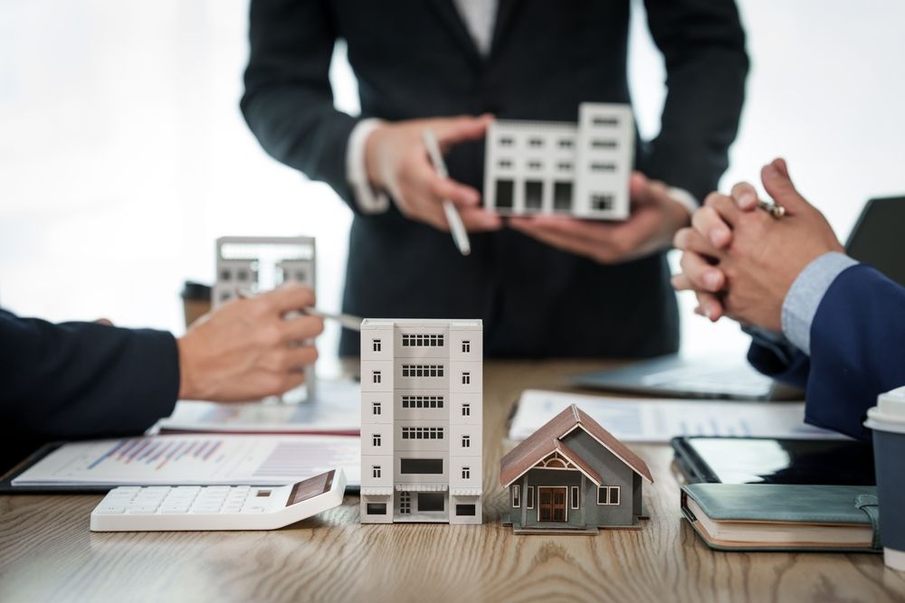 Real estate agents discussing property models at a table; office setting.
