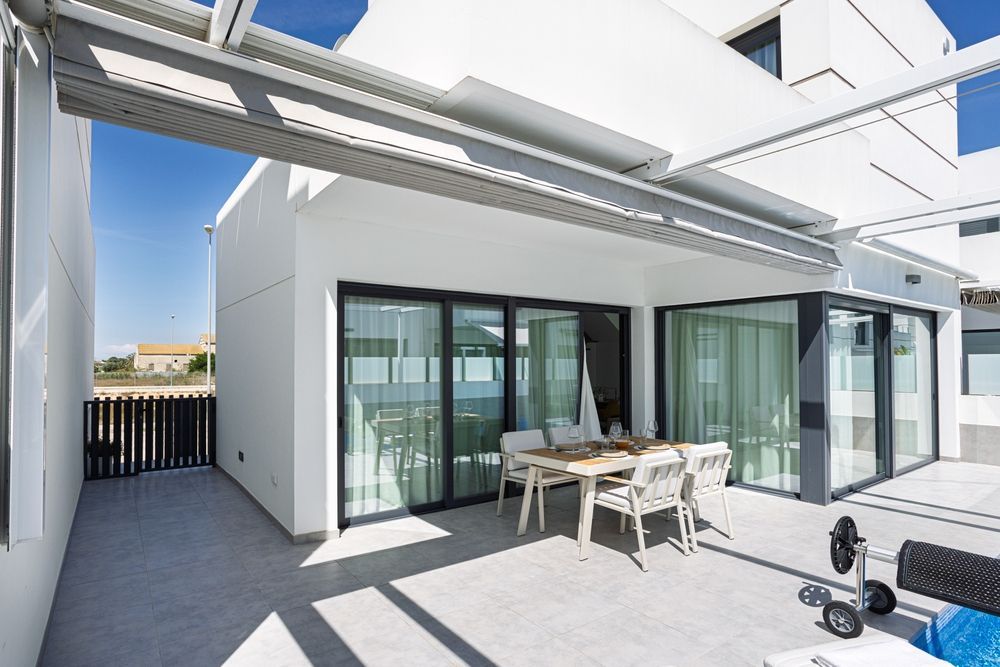 White modern patio with glass doors, outdoor dining set, and partial awning.