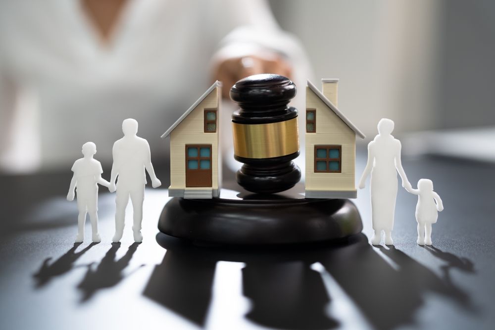 Divorce settlement concept: gavel, house, family cutouts, on black surface.