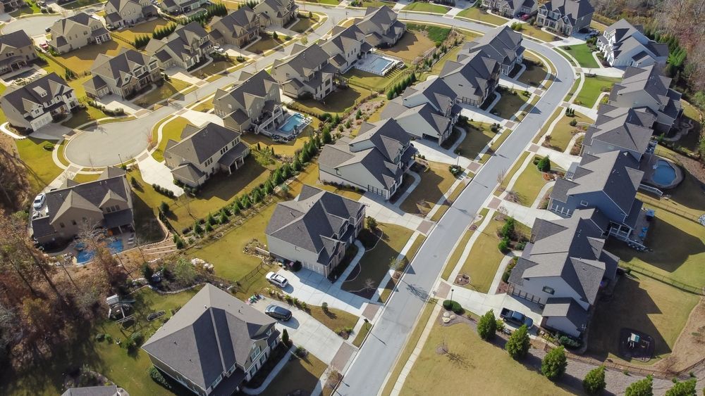 Aerial view of suburban houses with matching roofs and manicured lawns along a curved street.