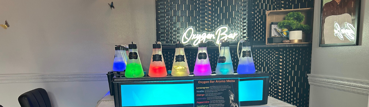 A brightly lit bar with colorful beverages in science beakers. A neon sign above it reads “Oxygen Bar.”