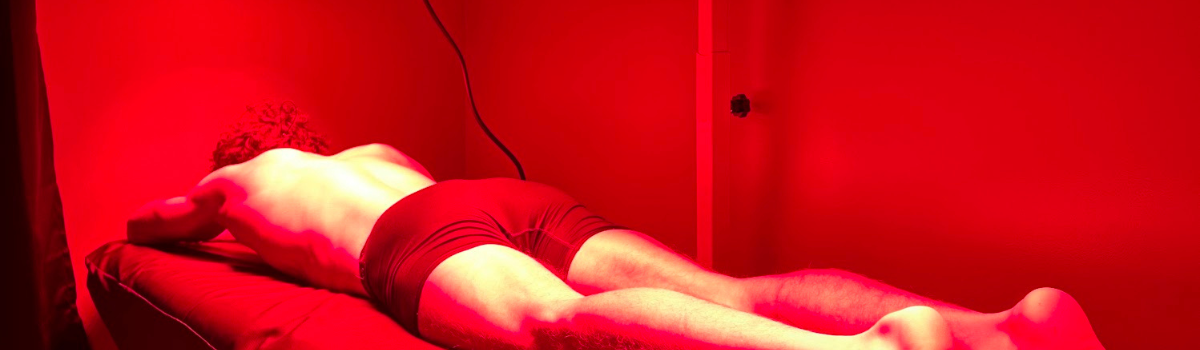 Person lying face down on a red surface, lit by red light.