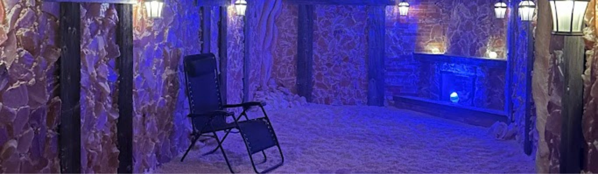A salt room illuminated with blue light. A chair sits in the center. The walls are textured with a brown color.