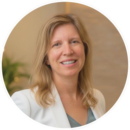 Woman in a white blazer smiles, standing in front of a neutral backdrop.