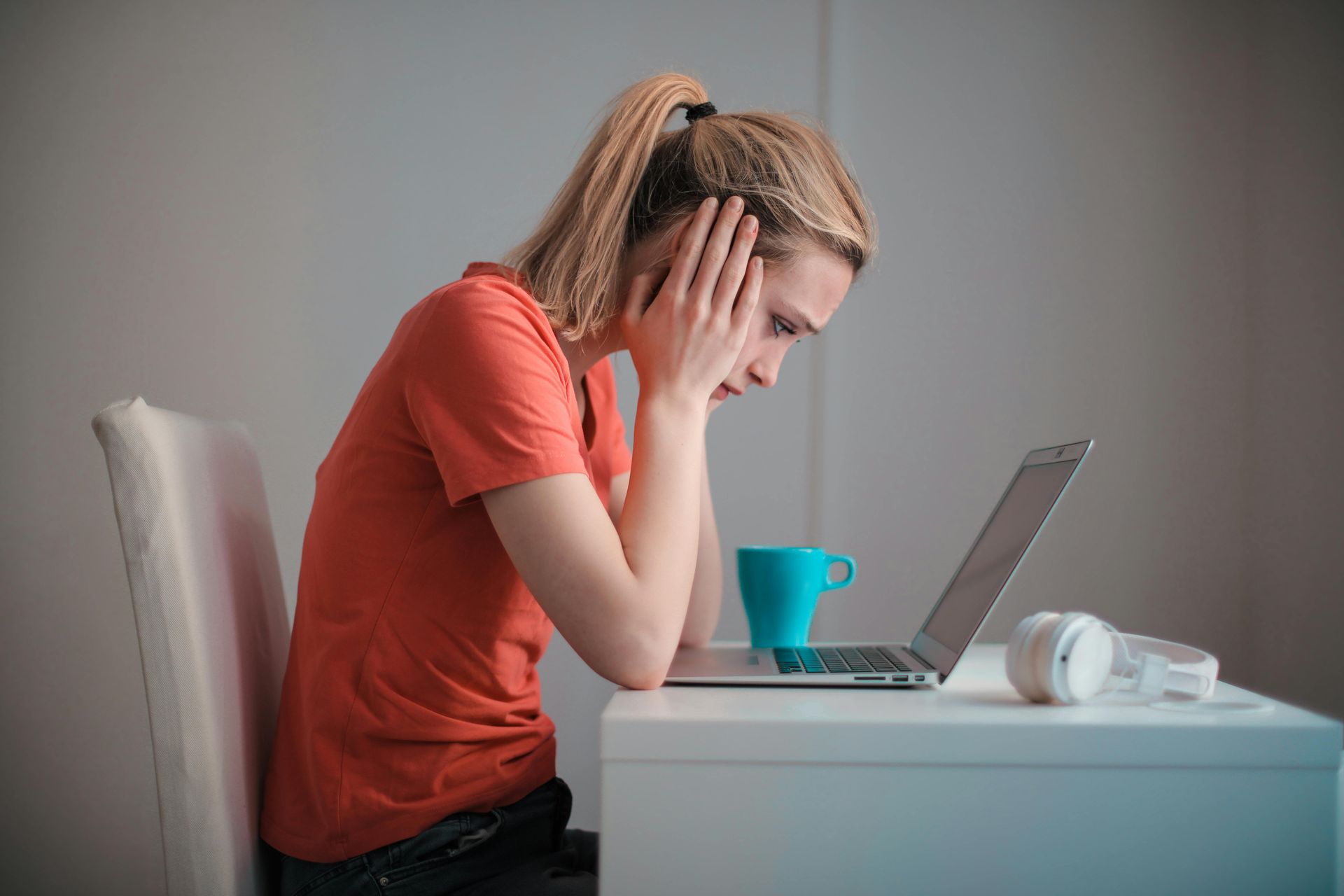 A woman is sitting at a desk with a laptop and headphones.