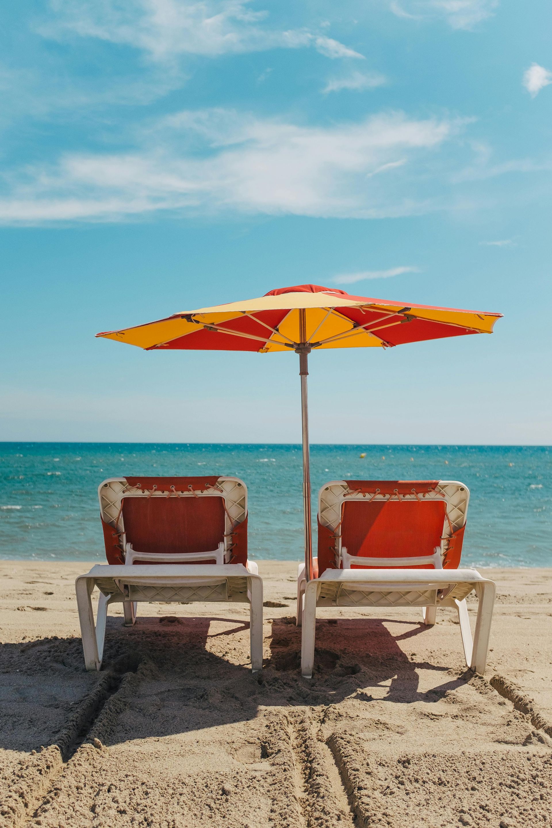 Two lounge chairs under an umbrella on a beach.