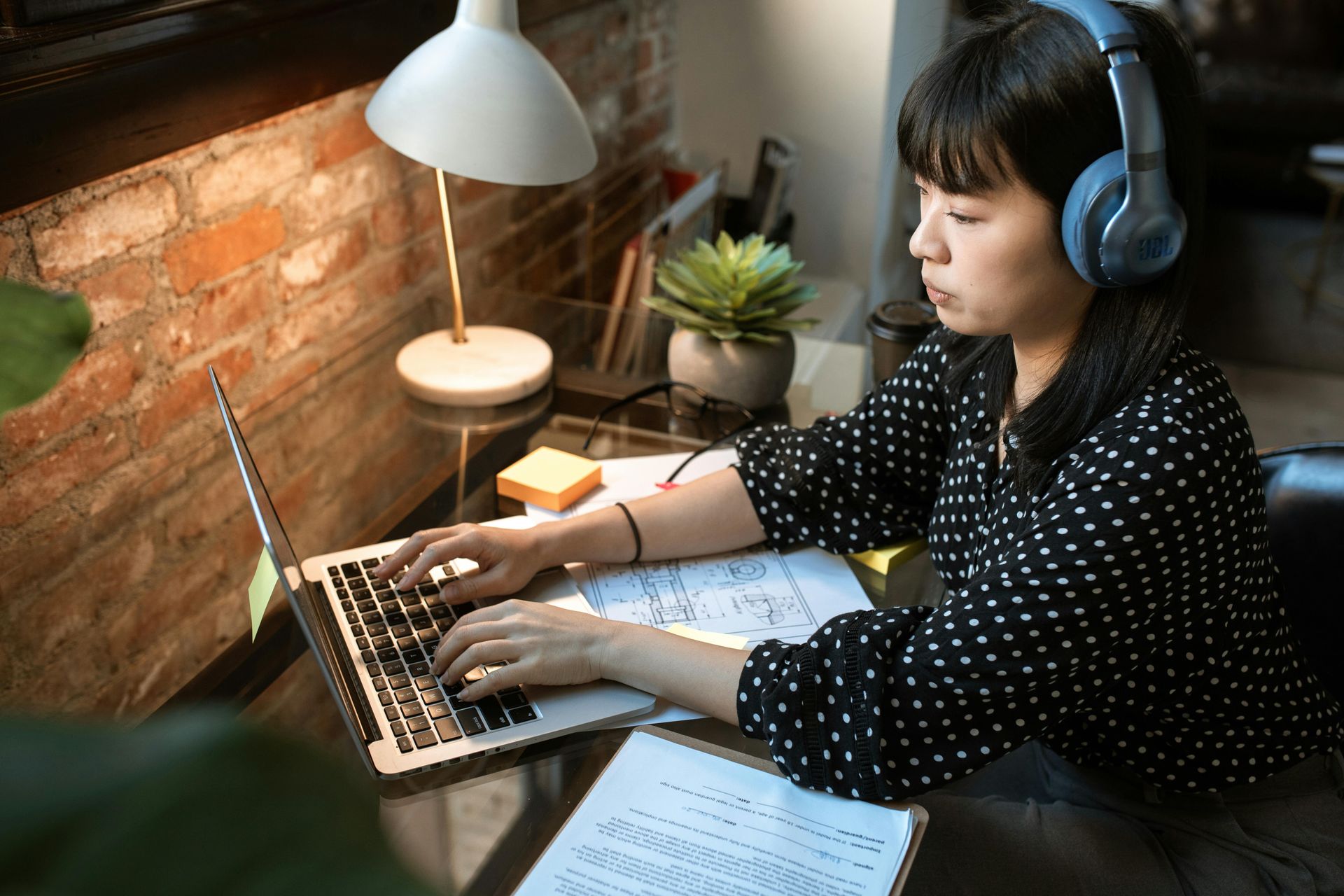 A woman wearing headphones is typing on a laptop computer.